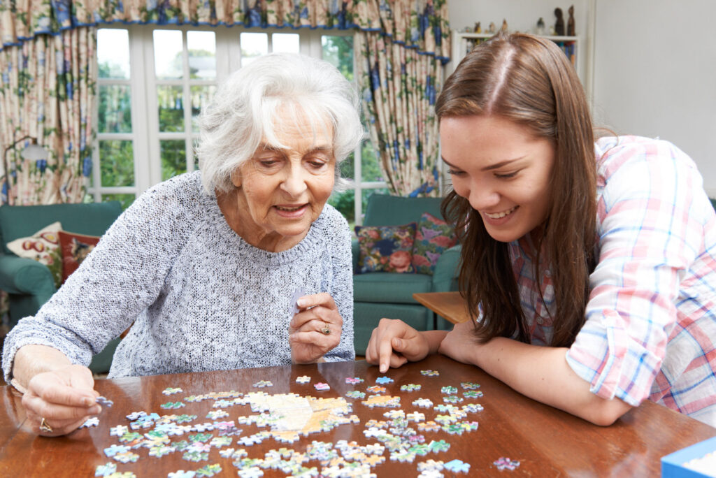 Elderly woman with Alzheimer's at Bel Air Assisted Living completing a puzzle with the assistance of a caregiving team member